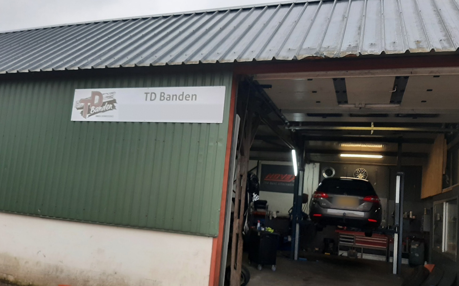 De voorkant van de werkplaats aan de Marsweg met het bord TD Banden en een auto op de brug